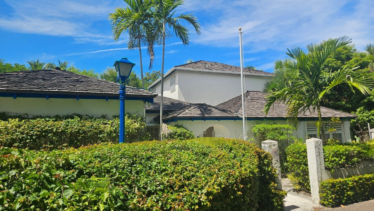 Bungalow with a shingle roof behind hedges