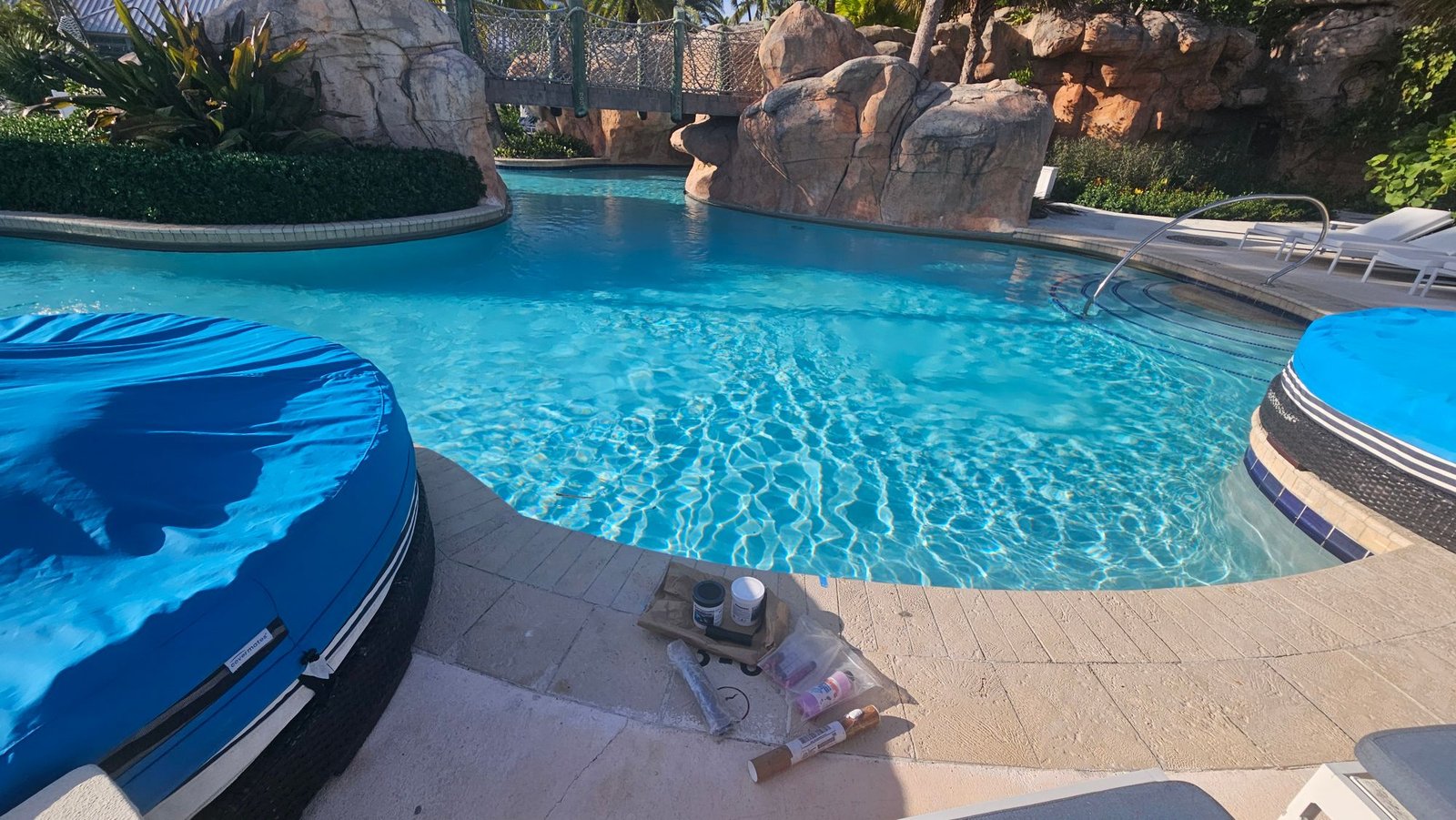 Resort lagoon pool with rock features and a rope bridge, with repair materials on the deck