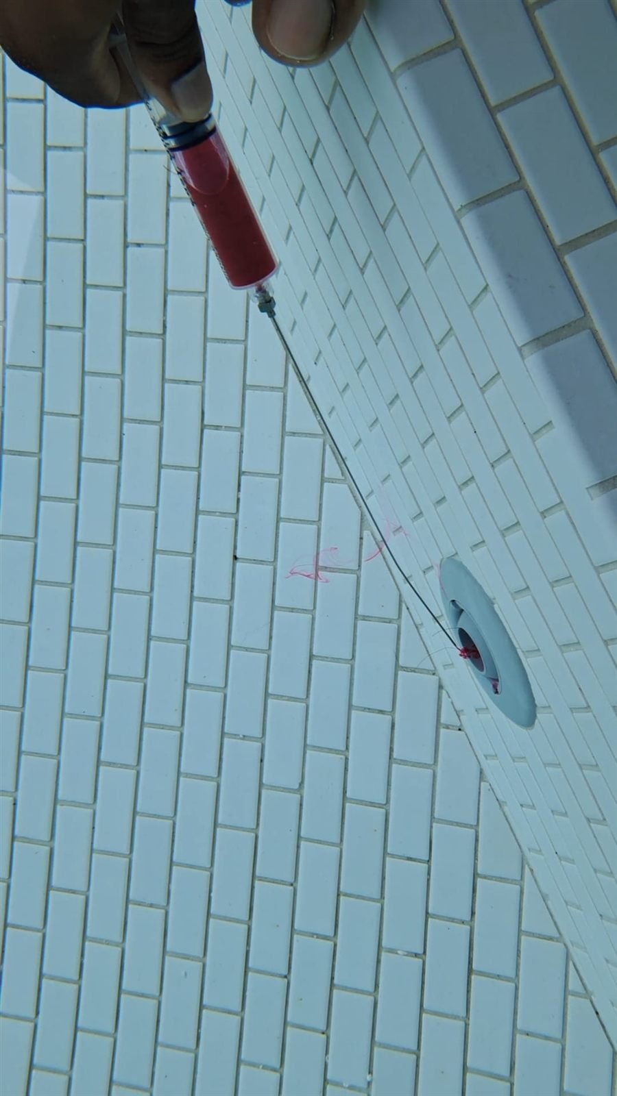 Dye released from a syringe at a pool fitting to trace a leak